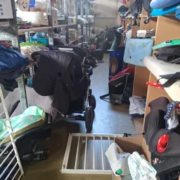 Rommelig interieur van kringloopwinkel met kinderwagens, stellingen en diverse spullen
