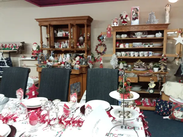 Winkelinterieur met houten meubels, tafeldecoratie en kersversiering, uitgestalde serviesgoed en decoratieve items op rekken
