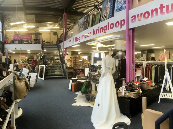Winkelvloer met kledingrekken, etalagepoppen en diverse spullen; paarse winkelbanners zichtbaar