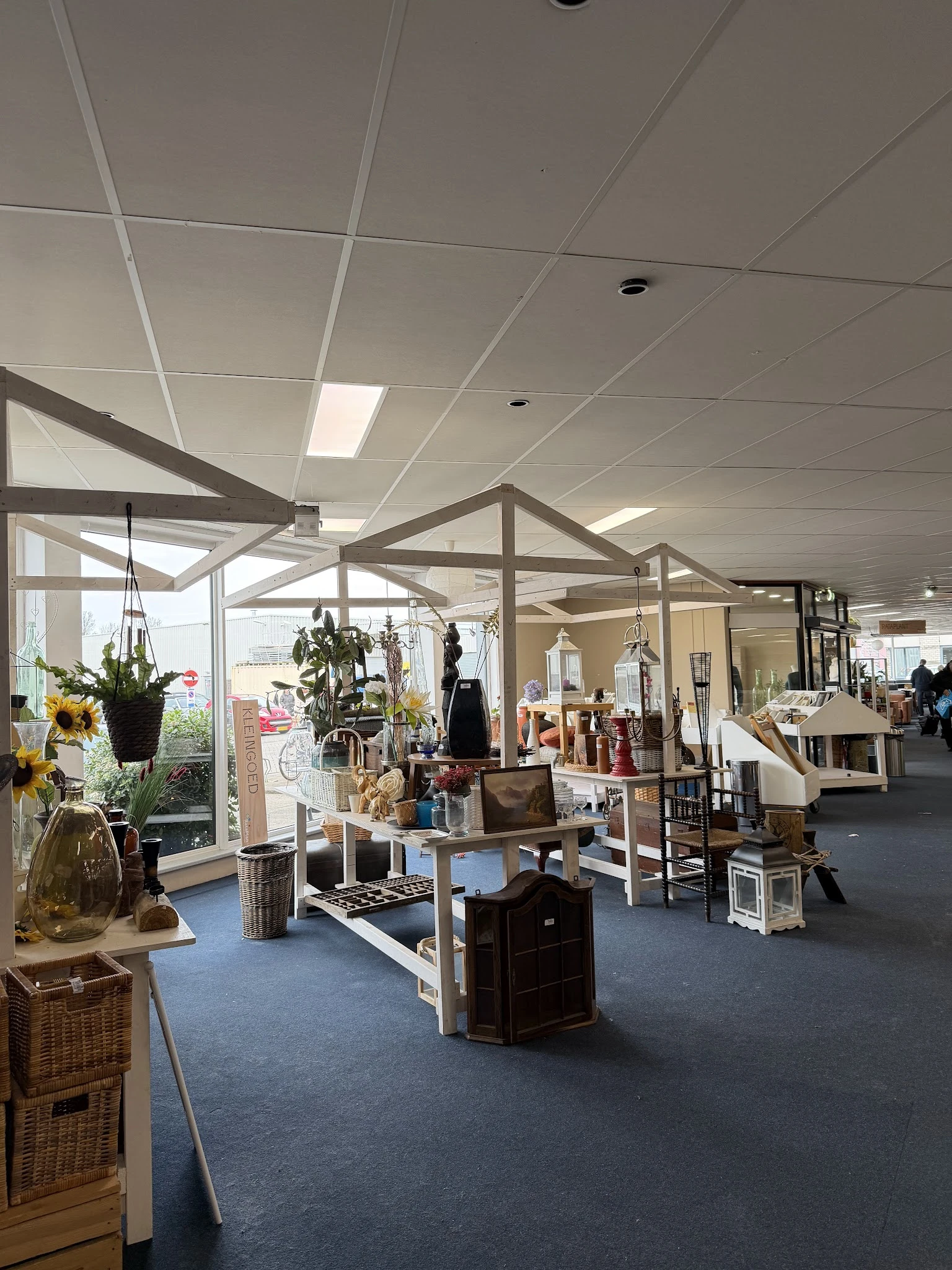 Ruim interieur van kringloopwinkel met stellingen, meubels, hangkleding en inrichtingsobjecten onder kasseinplafond met dagli