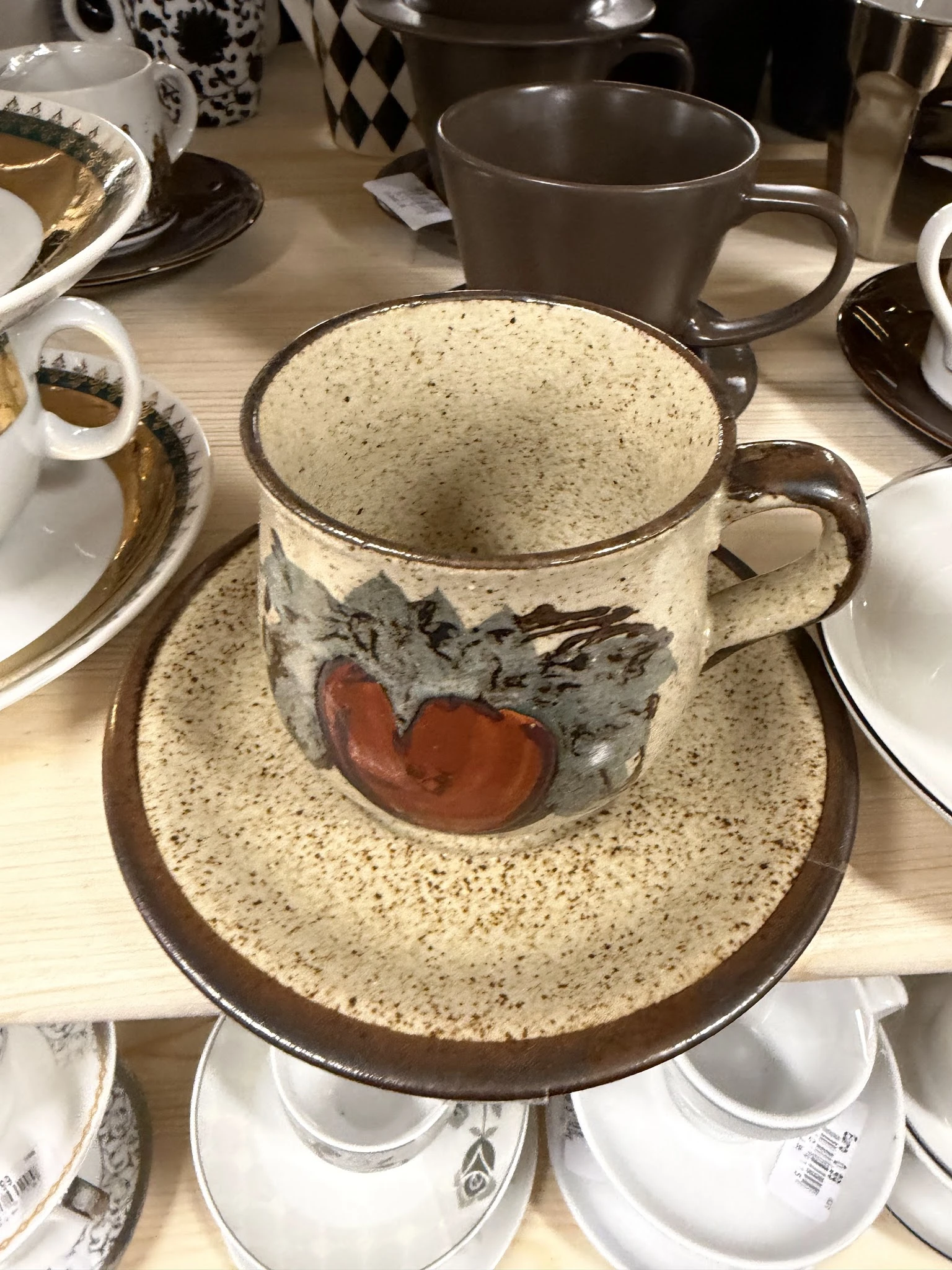 Tweedehands servies: een beige gespikkelde kop en schotel met rood-grijs decoratief motief
