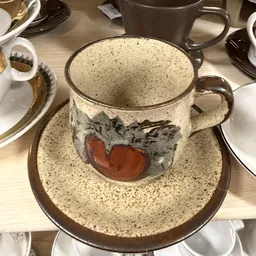 Tweedehands servies: een beige gespikkelde kop en schotel met rood-grijs decoratief motief