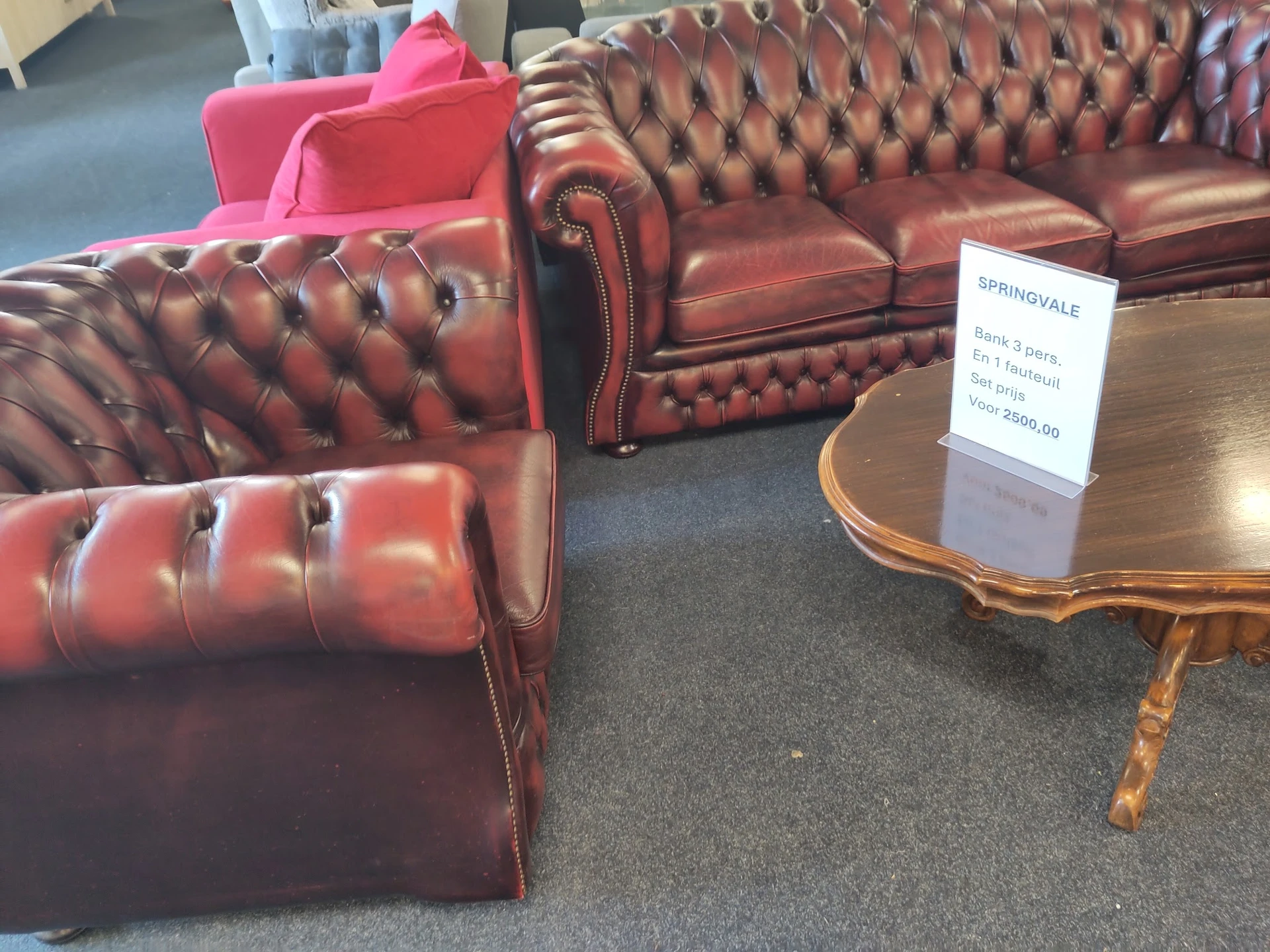 Rode Chesterfield-fauteuils en -banken in de winkelruimte met een prijskaartje