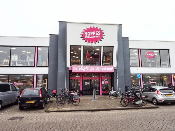 Gevel van kringloopwinkel Noppes met roze logo, grote ramen en ingang met fietsen ervoor geparkeerd