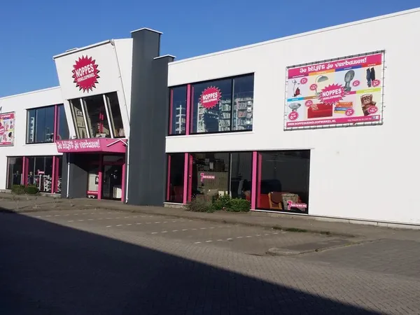 Witte gevel van kringloopwinkel Noppes met roze accenten, grote ramen en uithangeborden