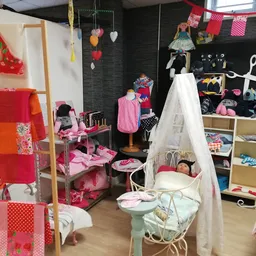 Speelgoedhoek met poppenhuis, pop en accessoires, kasten met speelgoed en kleding tegen zwarte muur met rode decoratie
