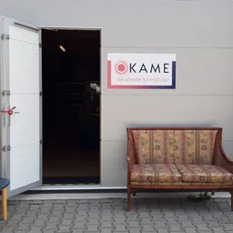 Winkelentree met open deur, logo van Okame de kleine kringloop, en vintage meubels op het terras