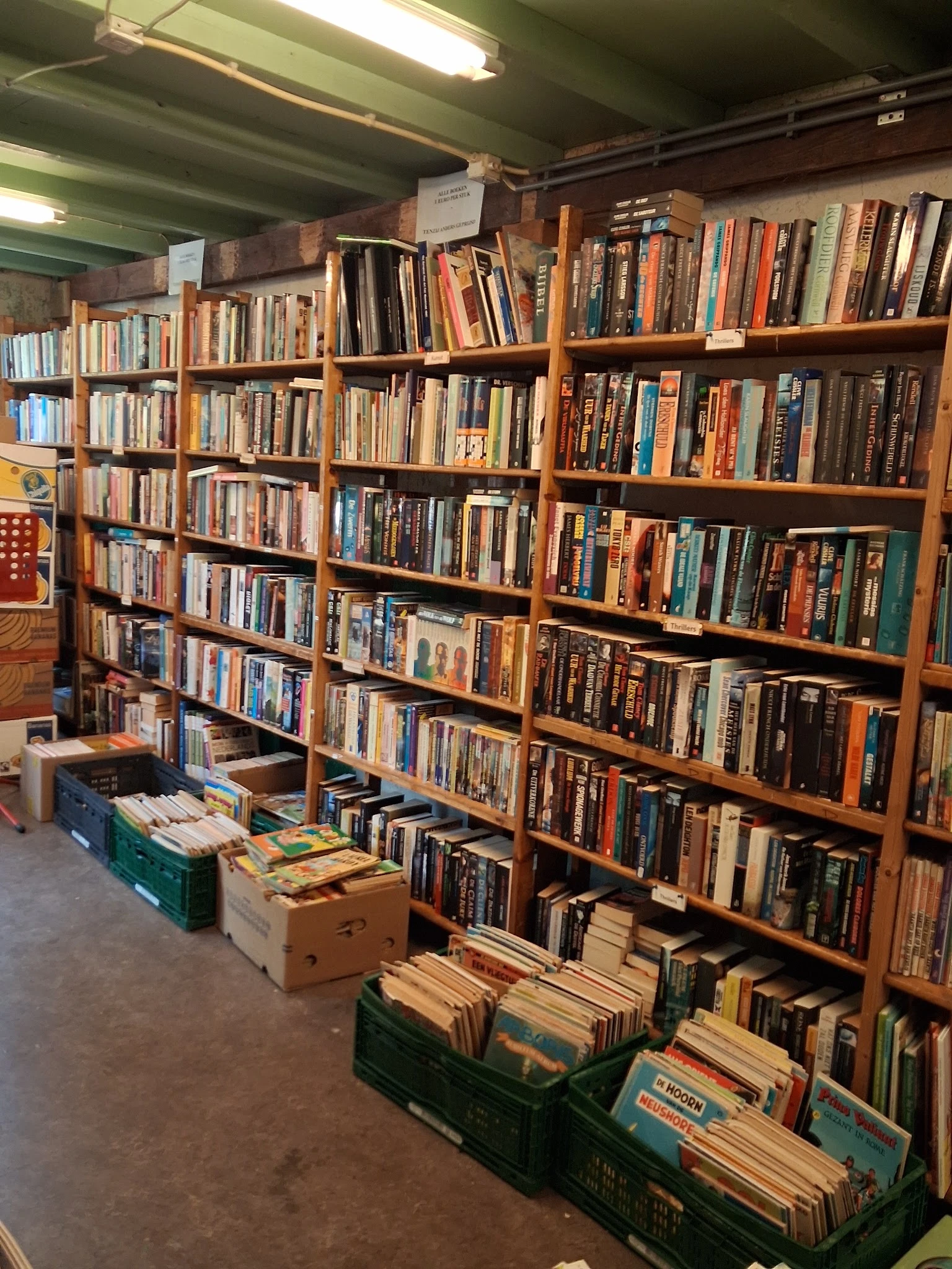 Houten stellingen vol met dvd's, blu-rays en cd's in een kringloopwinkel, met dozen met media op de grond