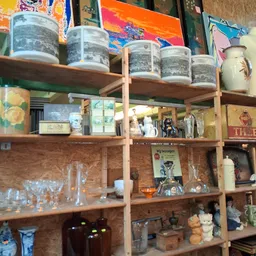 Houten stellingen met diverse tweedehands huishoudartikelen, glazen potten en decoratiespullen