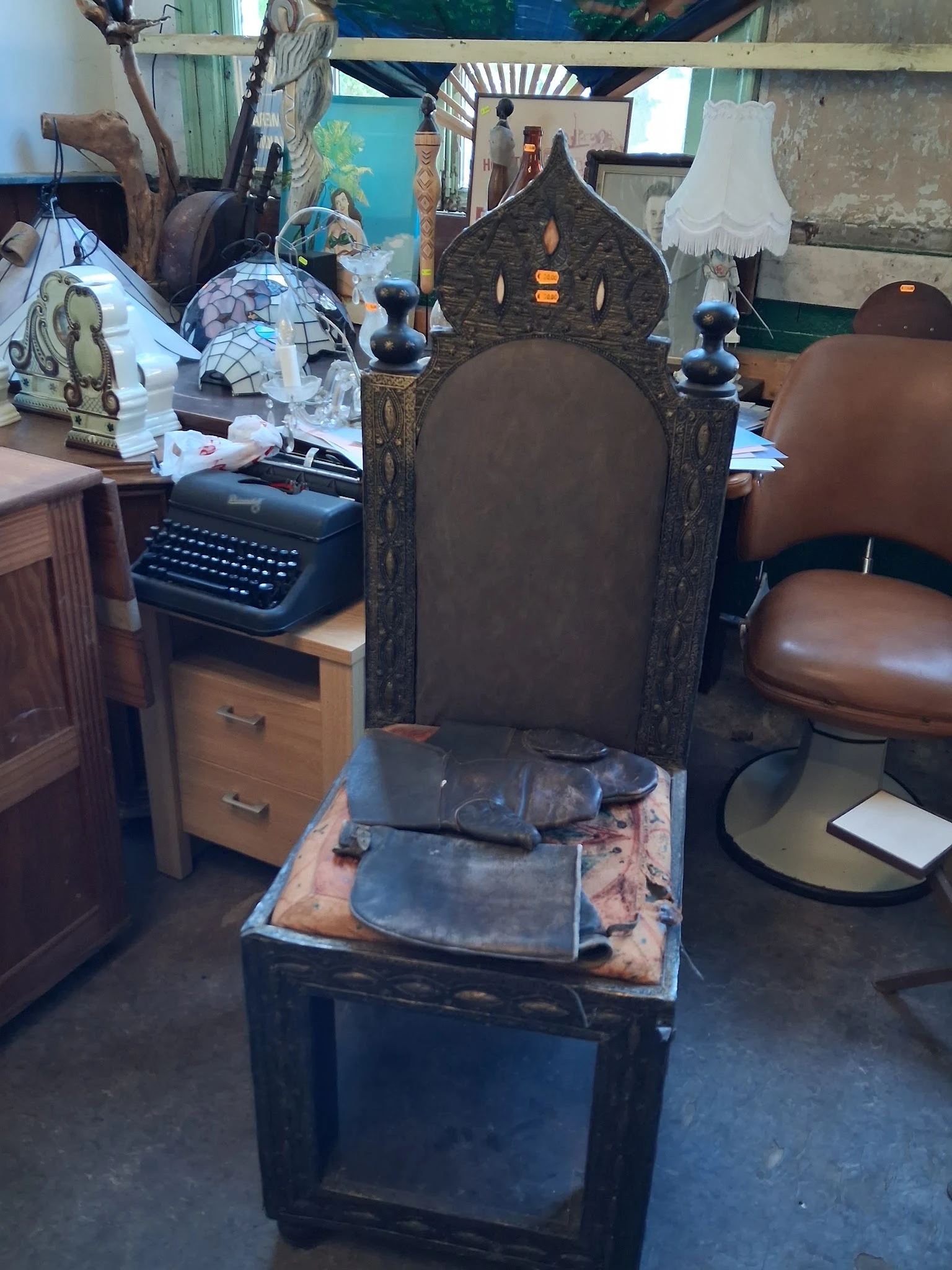 Zwarte vintage stoel met hoge rugleuning en bruine zitting, gedeeltelijk verpakt in plastic
