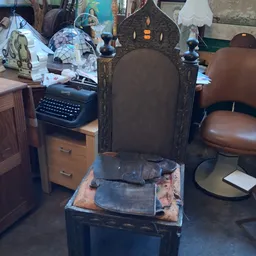 Zwarte vintage stoel met hoge rugleuning en bruine zitting, gedeeltelijk verpakt in plastic