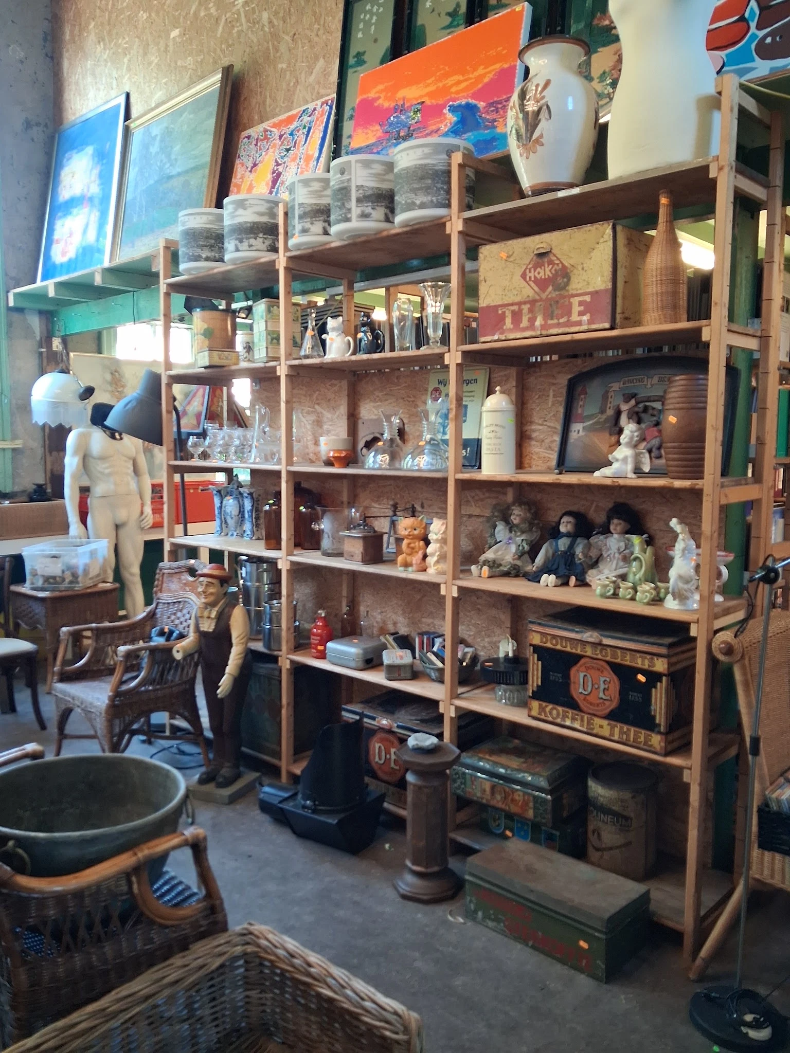 Houten stellingkast met diverse tweedehands spullen, decoratiestukken en voorwerpen; links een mannequin met kleding
