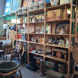 Houten stellingkast met diverse tweedehands spullen, decoratiestukken en voorwerpen; links een mannequin met kleding