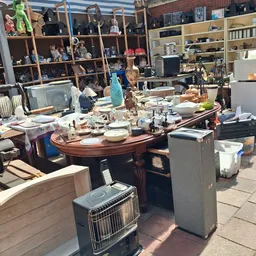 Binnenaanzicht van kringloopwinkel met houten bureaus, tafels, stellingen vol spullen en diverse meubels en huishoudartikelen