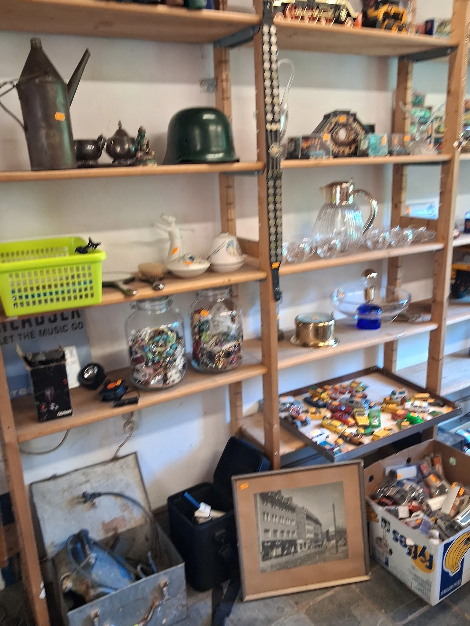 Houten stellingen met diverse tweedehands huishoudartikelen, serviesgoed, glazen en decoratieve voorwerpen