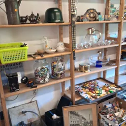 Houten stellingen met diverse tweedehands huishoudartikelen, serviesgoed, glazen en decoratieve voorwerpen