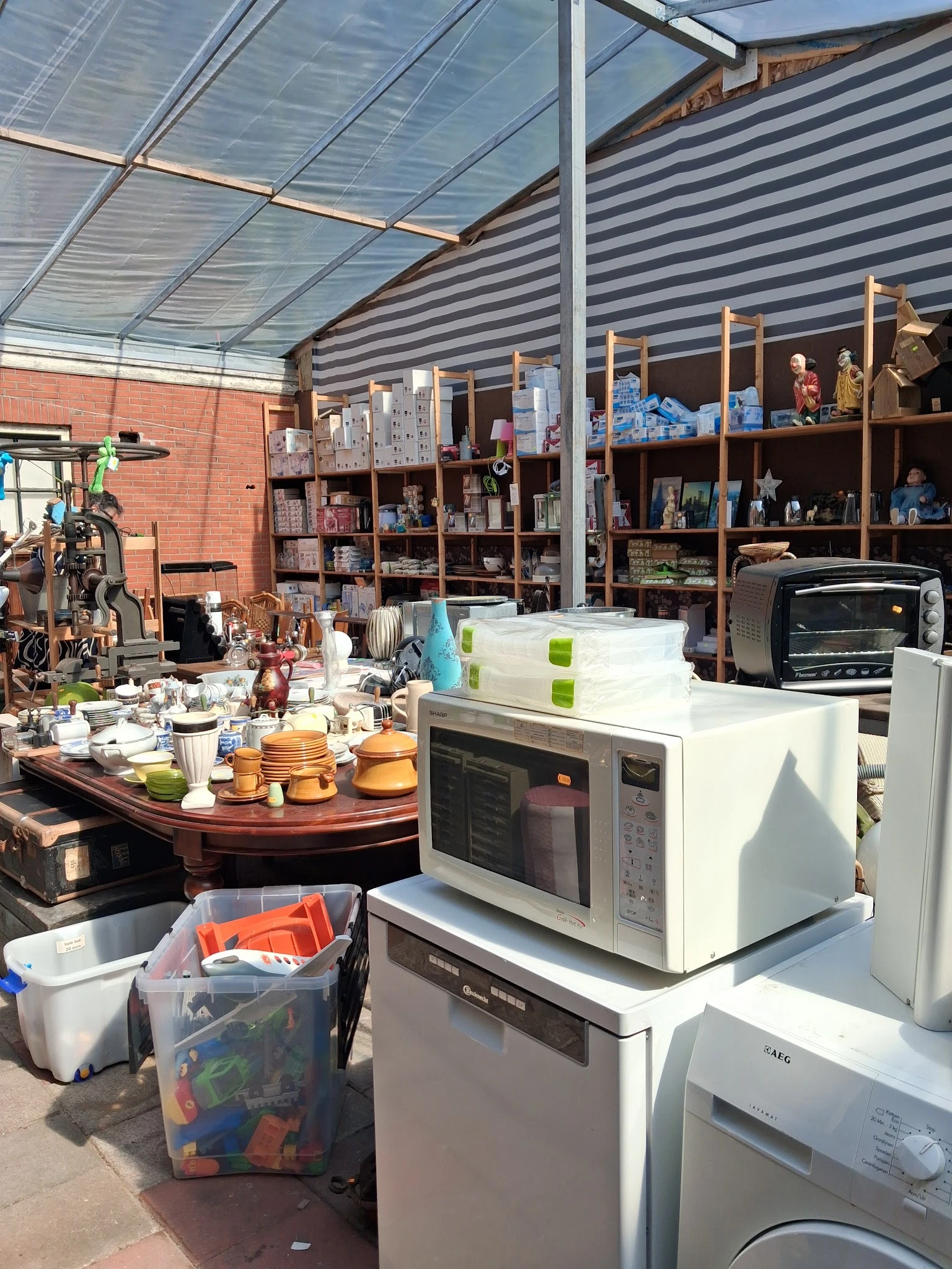 Uitgestalde huishoudelijke artikelen: servies, pannen, magnetron en keukenapparatuur op een werkblad en stellingen