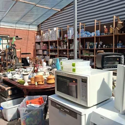 Uitgestalde huishoudelijke artikelen: servies, pannen, magnetron en keukenapparatuur op een werkblad en stellingen