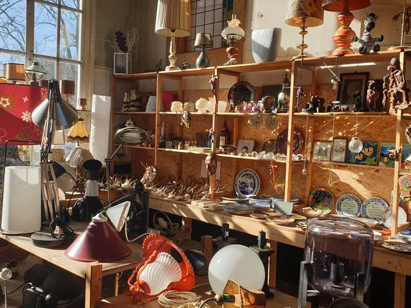 Winkelvloer met houten stellingen vol decoratieve spullen, lampen en servies in warme zonlicht