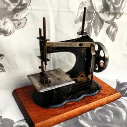 Antieke zwarte naaimachine op houten voetje tegen achtergrond met bloemenpatroon