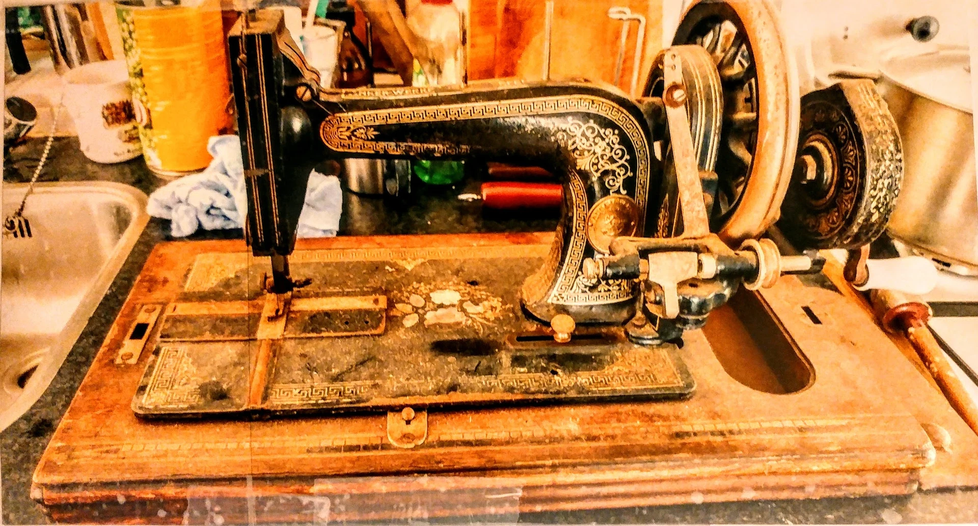 Antieke naaimachine met zwart en gouden ornamentering op houten tafel