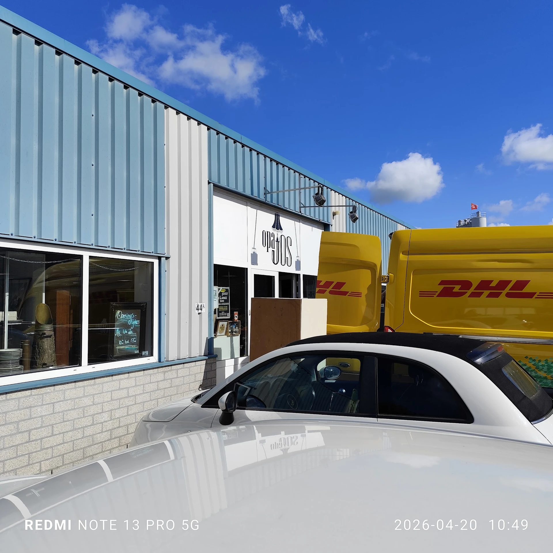 Gevel van kringloopwinkel met winkelpui en DHL-bezorgbus ernaast