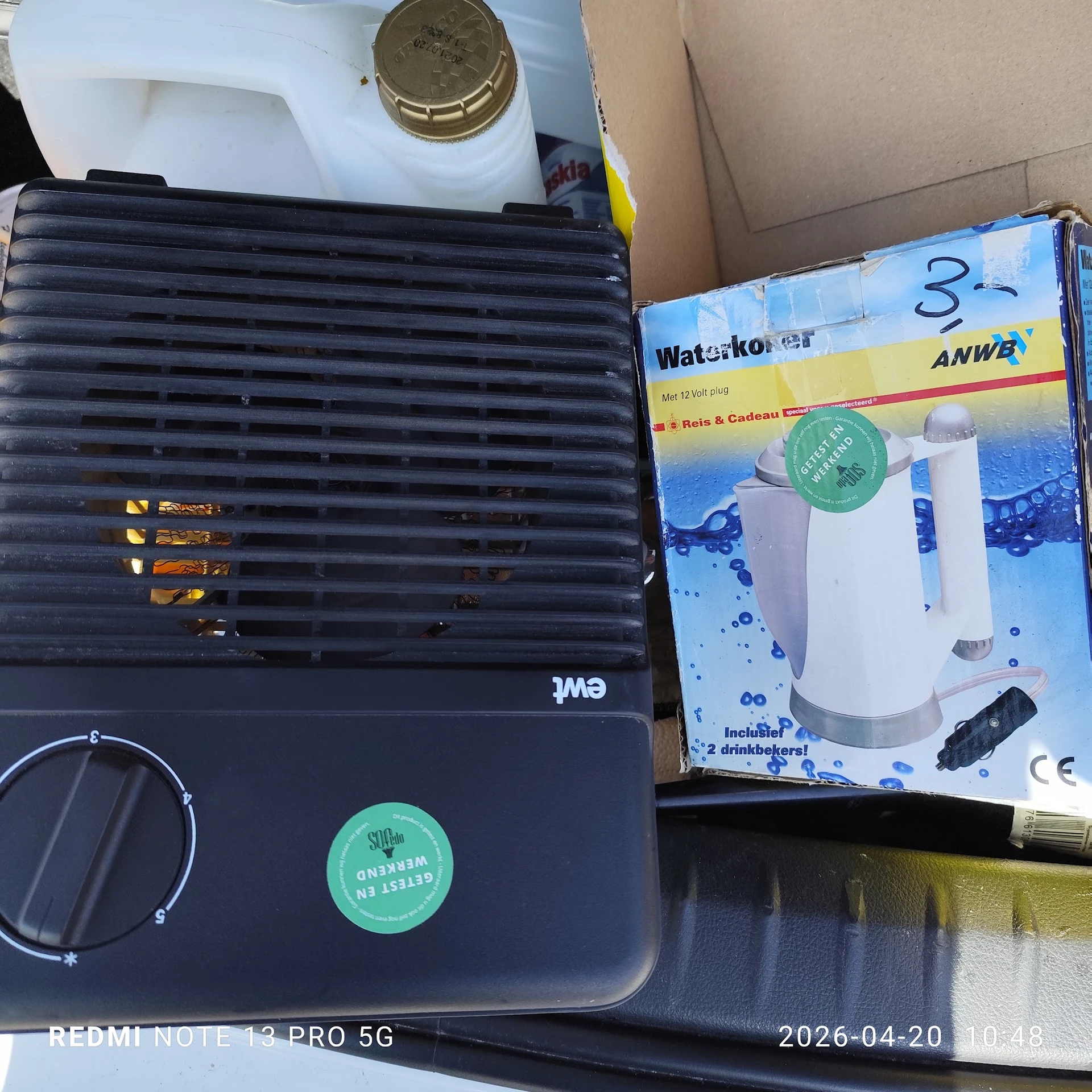 Tweedehands huishoudelijke artikelen: een zwarte ventilator en een waterkoker in verpakking