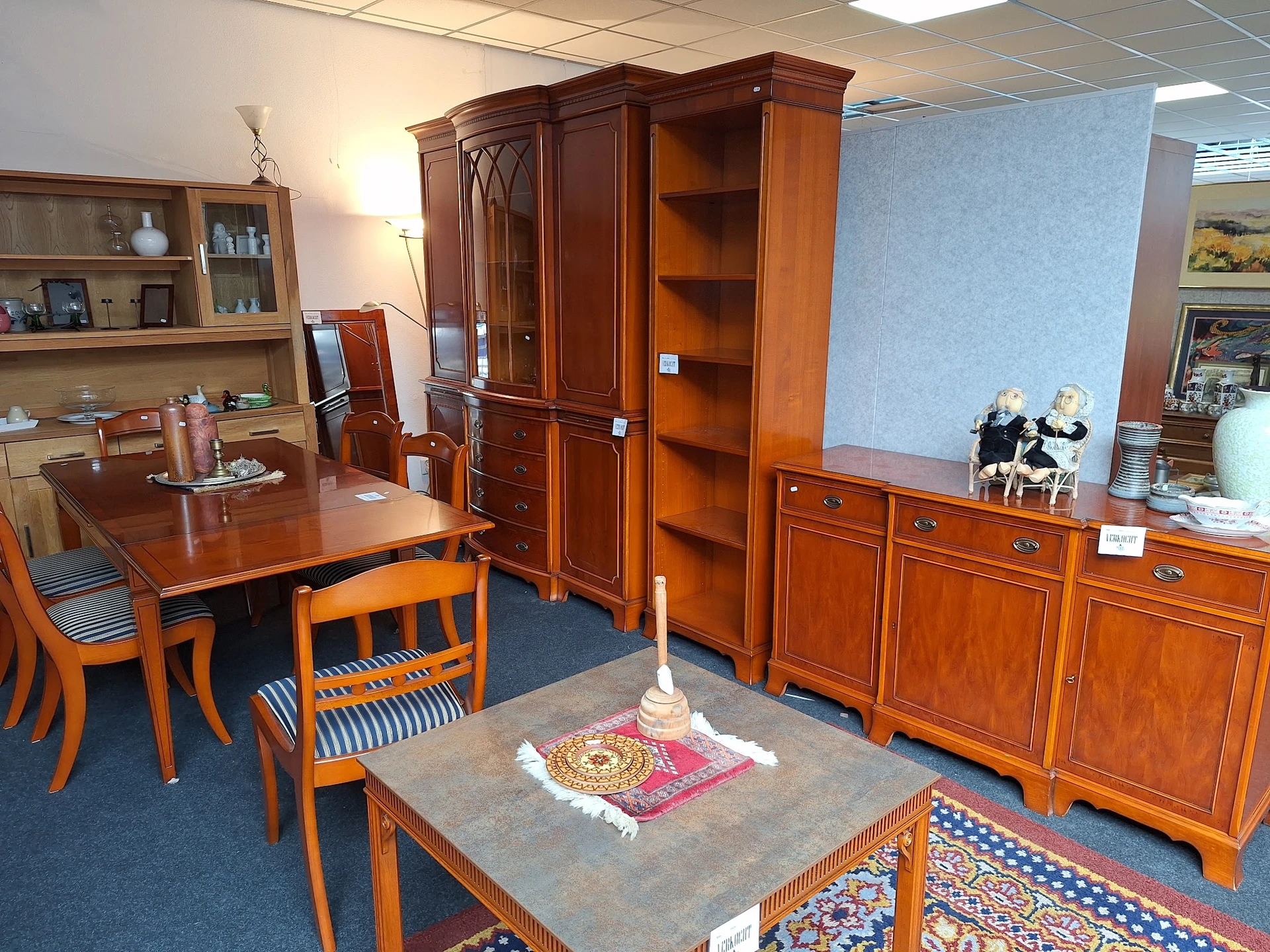Showroom met houten meubels: eettafel met stoelen, kasten en dressoirs op blauwe vloer met tapijten