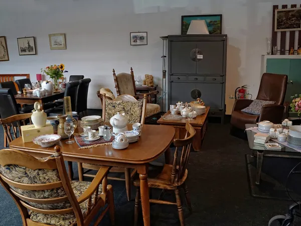 Ingerichte woonkamer met houten tafel, stoelen, servies en vintage meubels in kringloopwinkel
