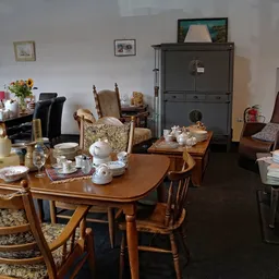 Woonkamer inrichting met houten eettafel, stoelen, serviesgoed en meubels in kringloopwinkel