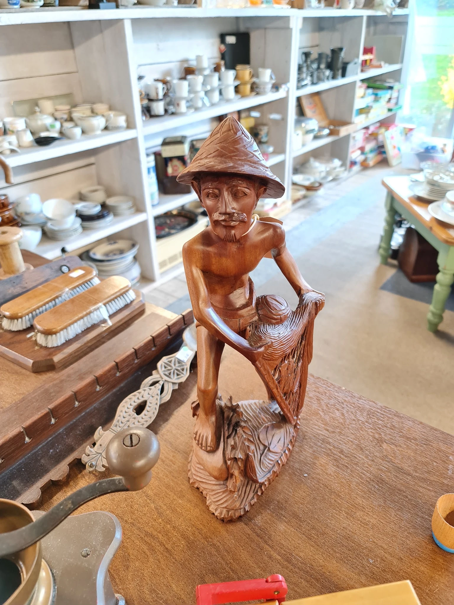 Houten beeldje van een man met hoed en snor, zittend op een stoel