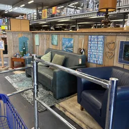 Inrichting van kringloopwinkel met grijze lederen zithoeken, decoratieve wandborden en houten wanden