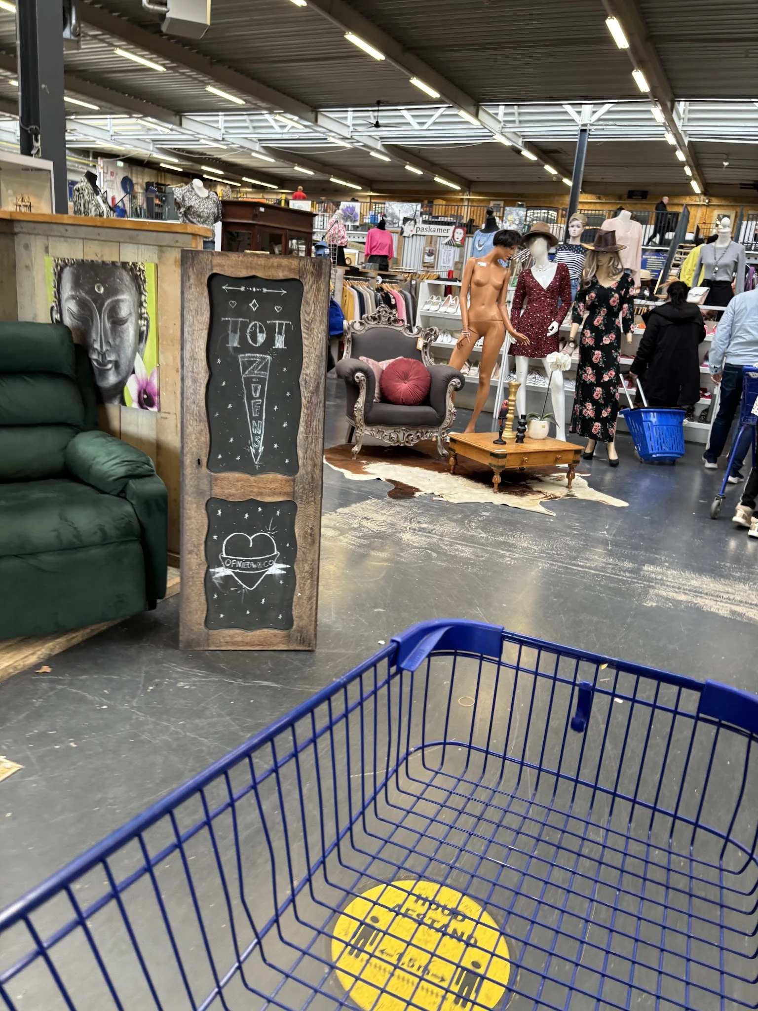 Winkelvloer met blauw winkelmandje, meubilair en kledingrekken met tweedehands spullen