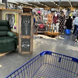 Winkelvloer met blauw winkelmandje, meubilair en kledingrekken met tweedehands spullen