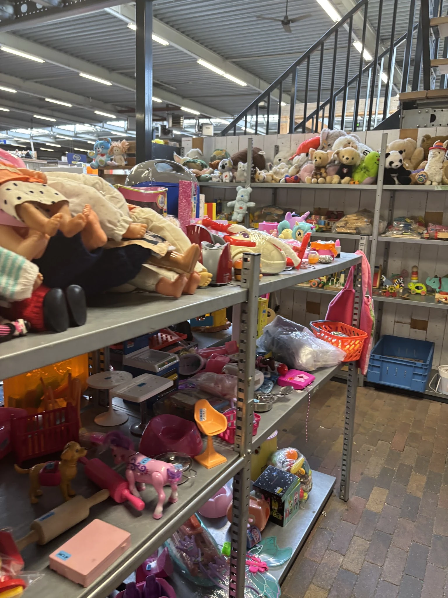 Metalen stellingen volgestapeld met speelgoed, knuffels en diverse huishoudelijke artikelen in een kringloopwinkel
