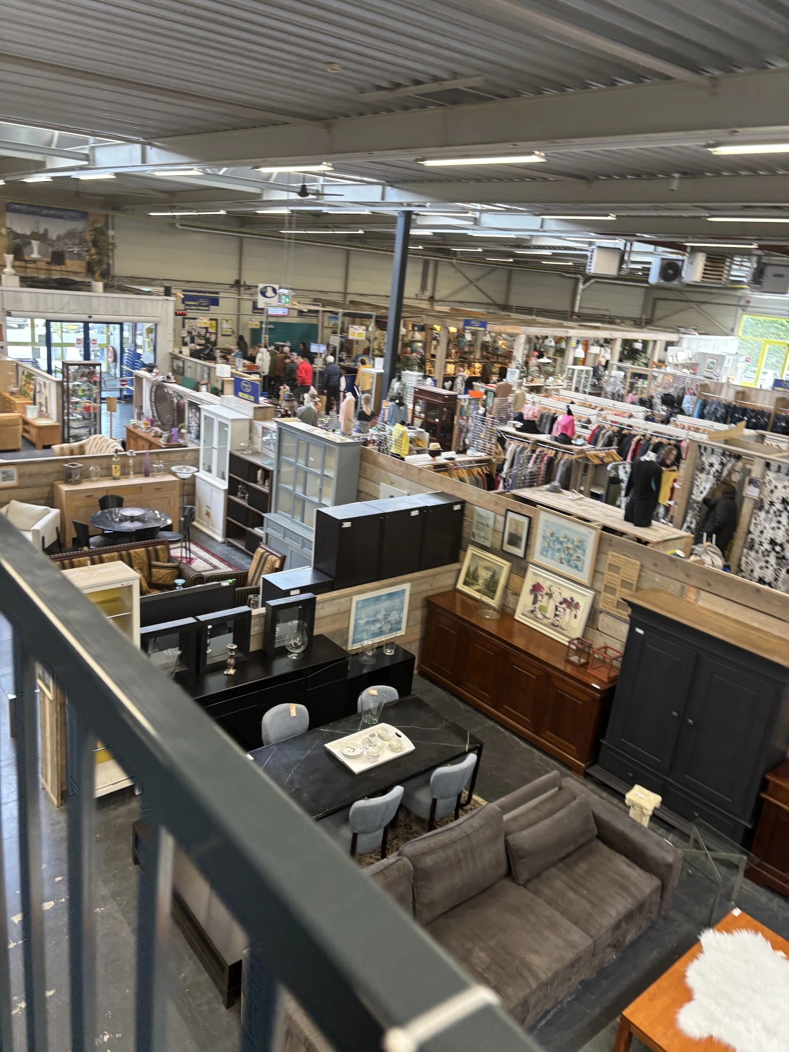 Overzicht van kringloopwinkel met verschillende afdelingen, meubilair, kunstwerken, kleding en diverse tweedehandsartikelen