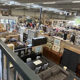 Overzicht van kringloopwinkel met verschillende afdelingen, meubilair, kunstwerken, kleding en diverse tweedehandsartikelen