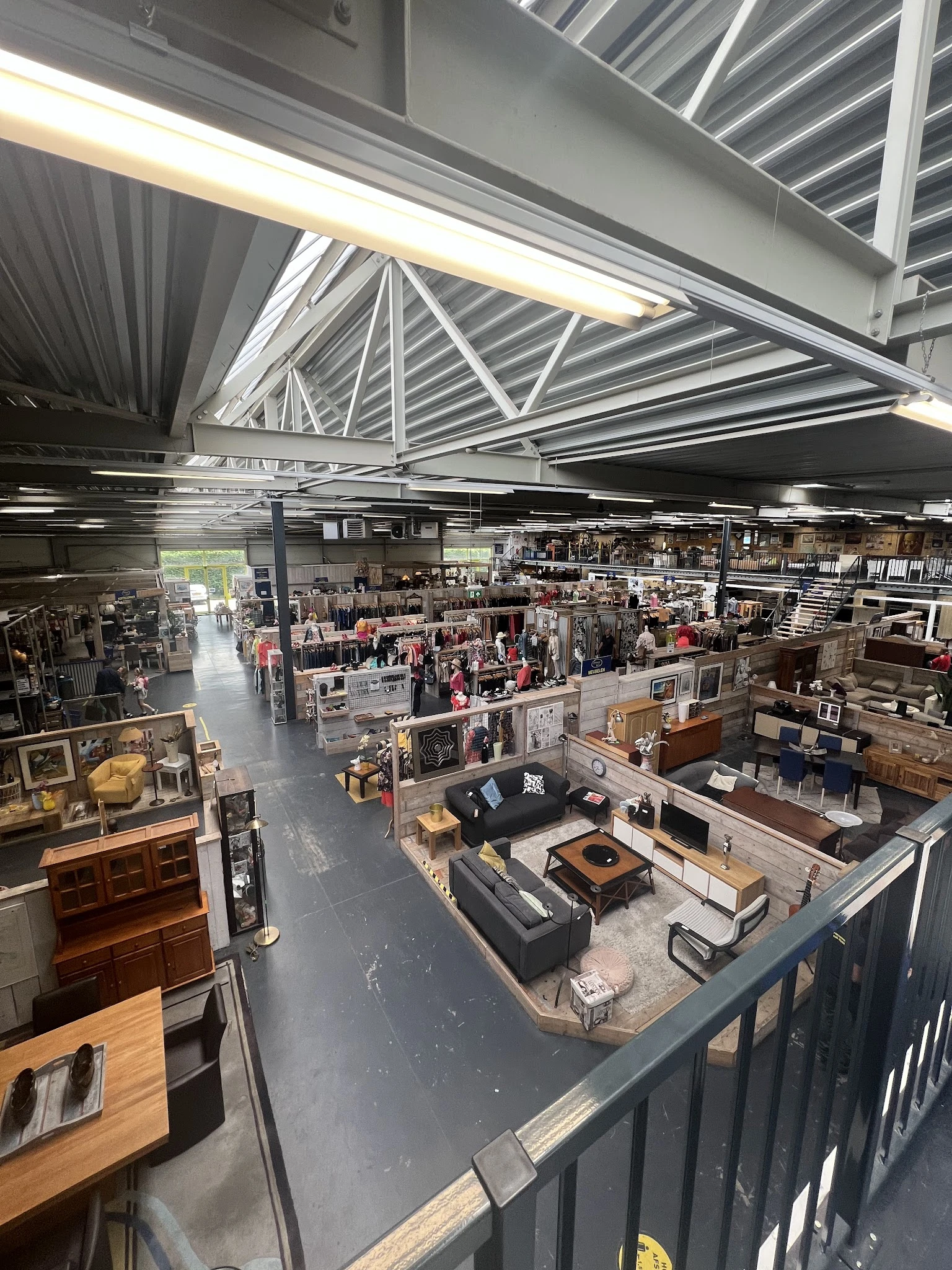 Overzicht van de winkelvloer met diverse afdeling, meubilair, kunstwerken en spullen onder een hoog plafond met dakramen