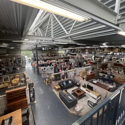 Overzicht van de winkelvloer met diverse afdeling, meubilair, kunstwerken en spullen onder een hoog plafond met dakramen