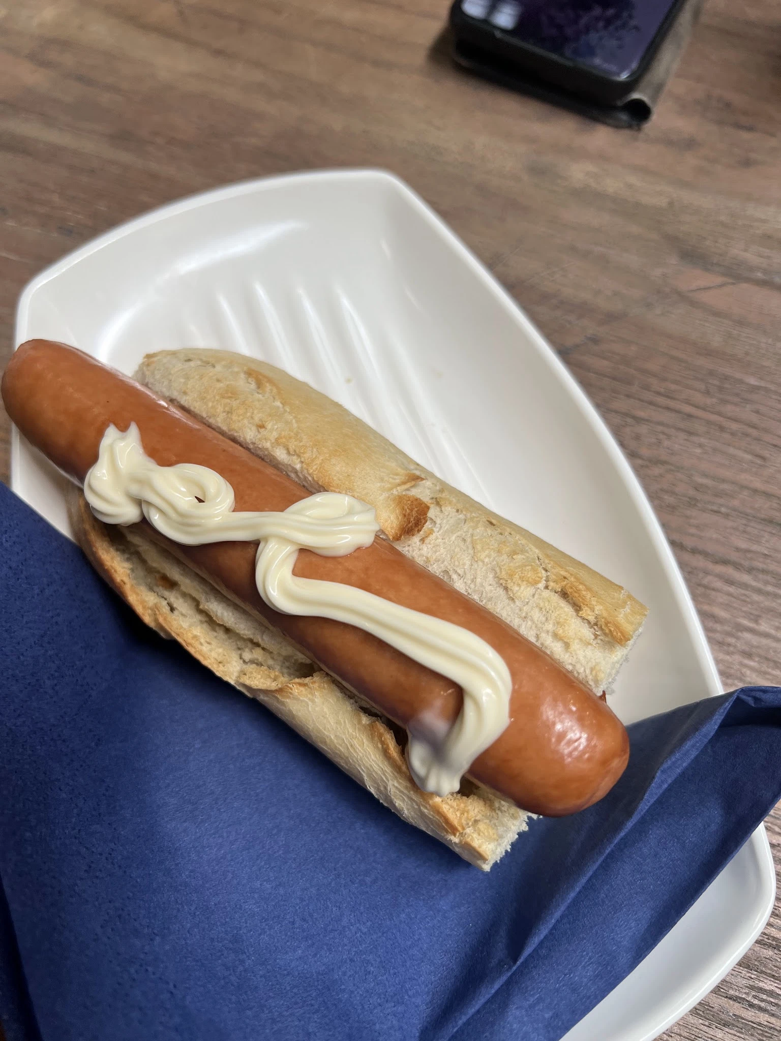 Hotdog met worst en mayonaise op een wit bordje