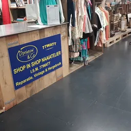 Binnenaanzicht van kringloopwinkel met kledingrekken, toonbank en informatiebord over reparaties