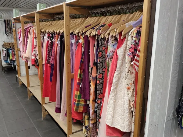 Houten rekken met kleurige tweedehands dameskledingstukken op hangers