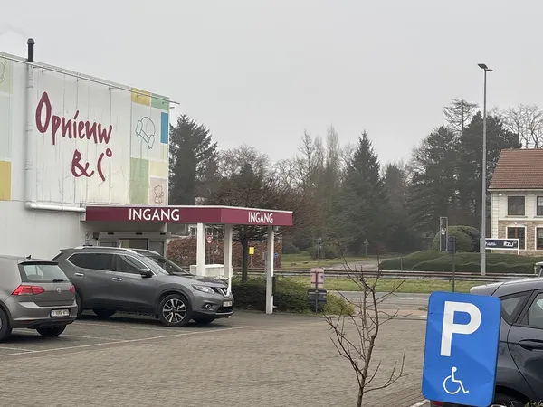 Gevel van kringloopwinkel Opnieuw & Co met ingang, parkeerplaats en handicapenparkeerplaats.