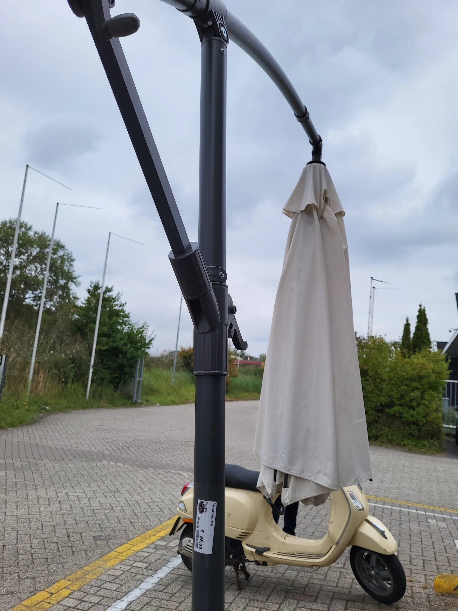 Zwarte parasol met beige parasoluiting op een voetpad buiten een winkel