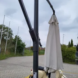 Zwarte parasol met beige parasoluiting op een voetpad buiten een winkel