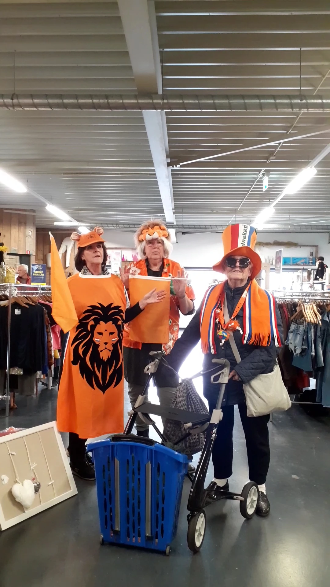 Drie vrijwilligers in oranje kleding en accessories poseren in de winkel