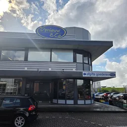 Voorgevel van kringloopwinkel Opnieuw & Co met blauwe gevel en parkeerplaats ernaast