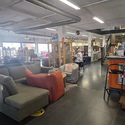 Winkelvloer met grijze en oranje zitmeubels, stellingen en afdelingen in een kringloopwinkel