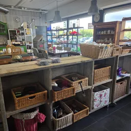 Winkelinterieur met zwarte stellingen gevuld met rieten manden, houten werkblad en houten stoelen, grote ramen met uitzicht
