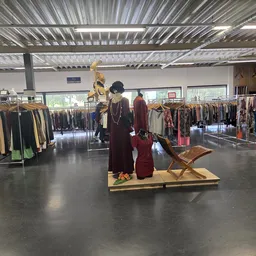 Ruime winkelruimte met kledingrekken en een etalagepop in rode jurk op een houten plateau